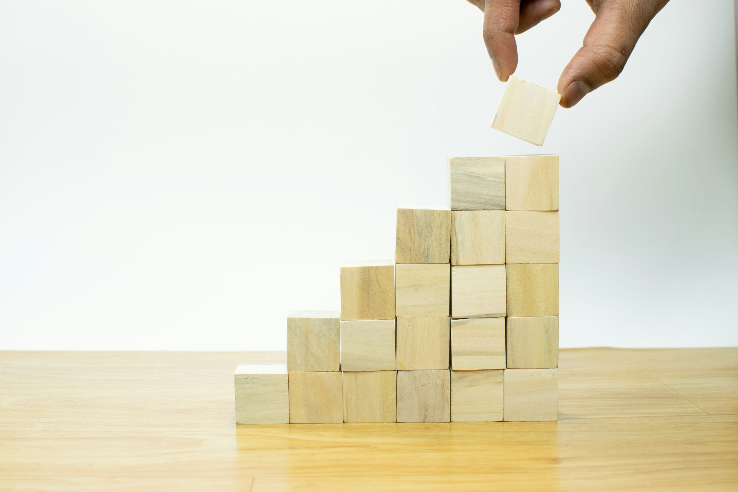 imagine-buddy-vsLbaIdhwaU-unsplash (1) A photo of a stack of blocks that forms steps. A person's thumb and forefinger are visible adding a block to the top.